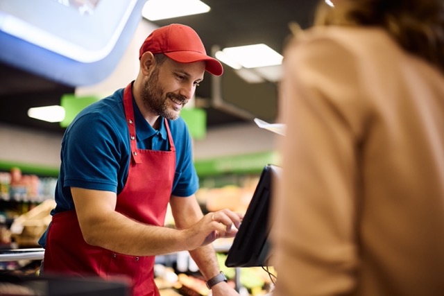 Independent grocery store owner using FlexRetail POS management platform showing real-time inventory dashboard and AI-powered insights at checkout lane