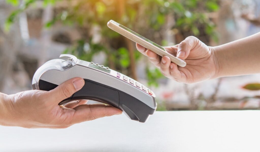 Grocery store customer tapping a mobile wallet to pay at an independent grocer's contactless payment terminal