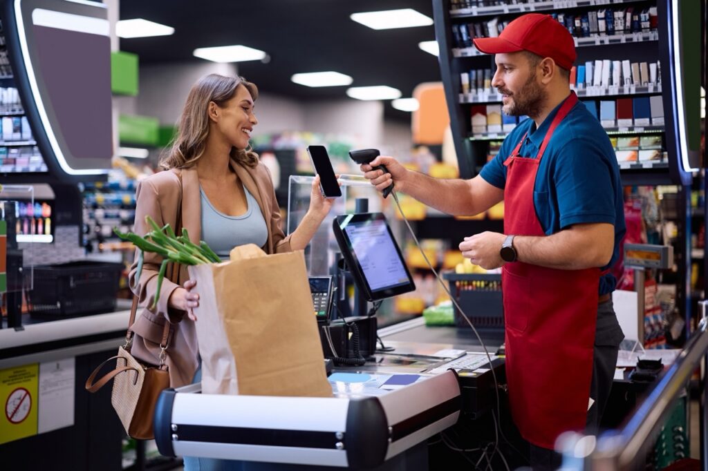 Grocery cashier scanning a digital coupon barcode from a customer's phone at checkout