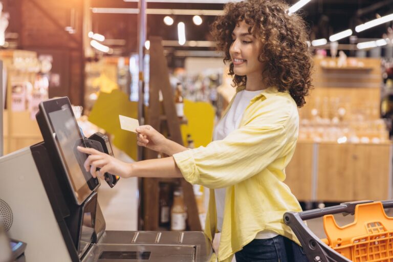 Shopper holding a card at a grocery self-checkout kiosk to complete an EBT split tender payment