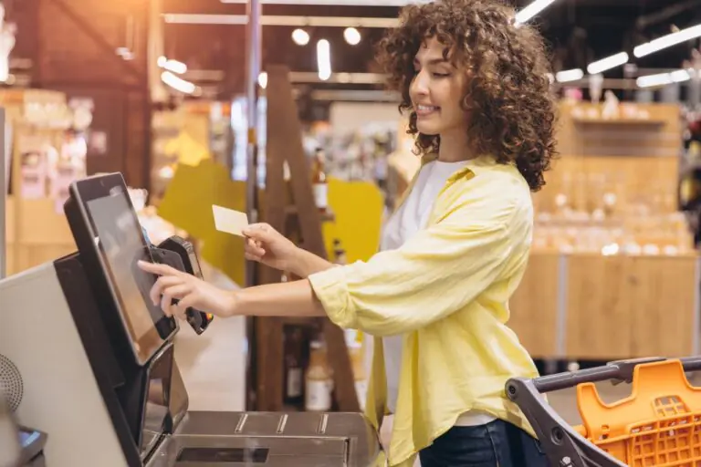 Shopper holding a card at a grocery self-checkout kiosk to complete an EBT split tender payment